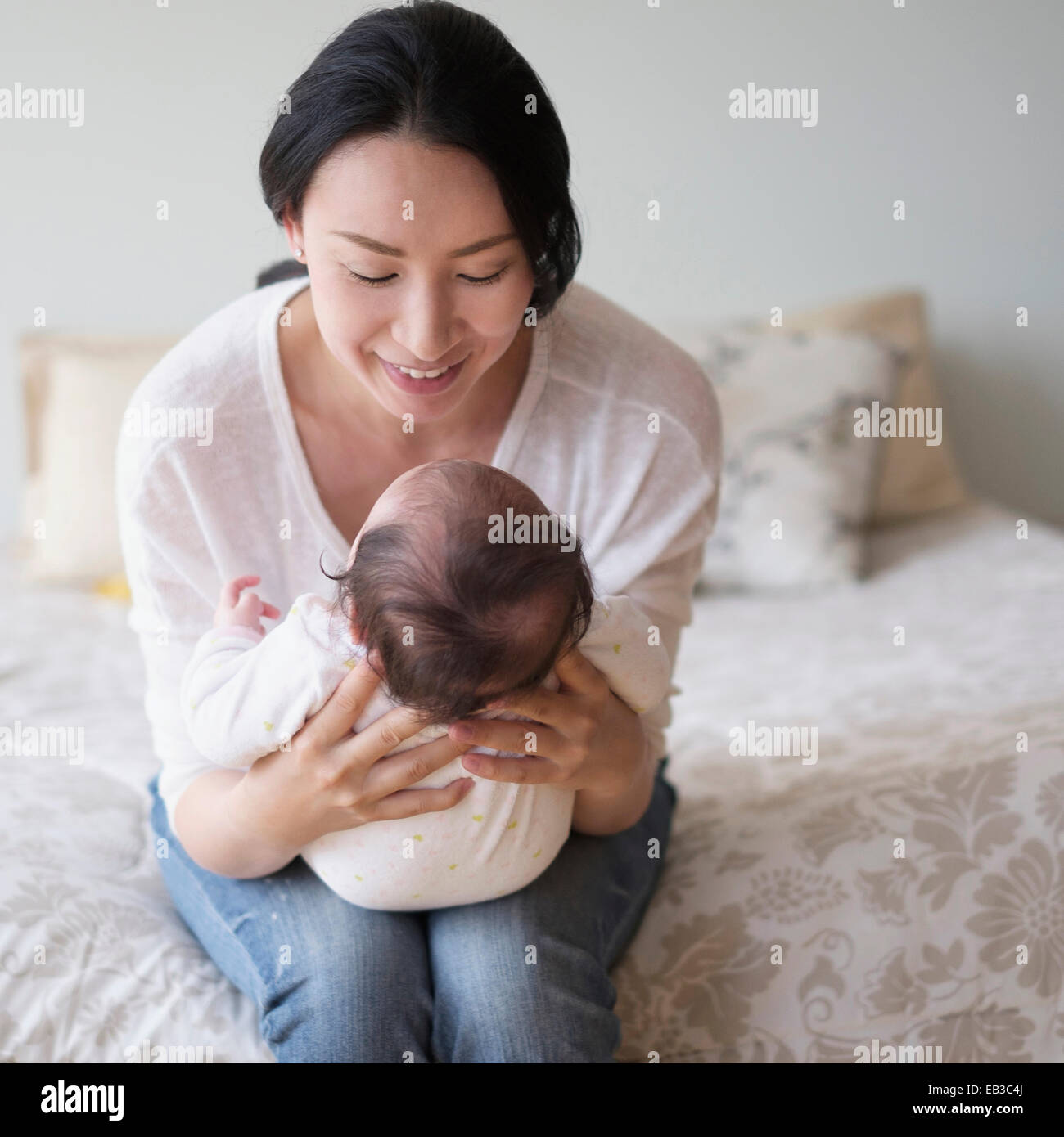 Asian mother holding baby on bed Stock Photo