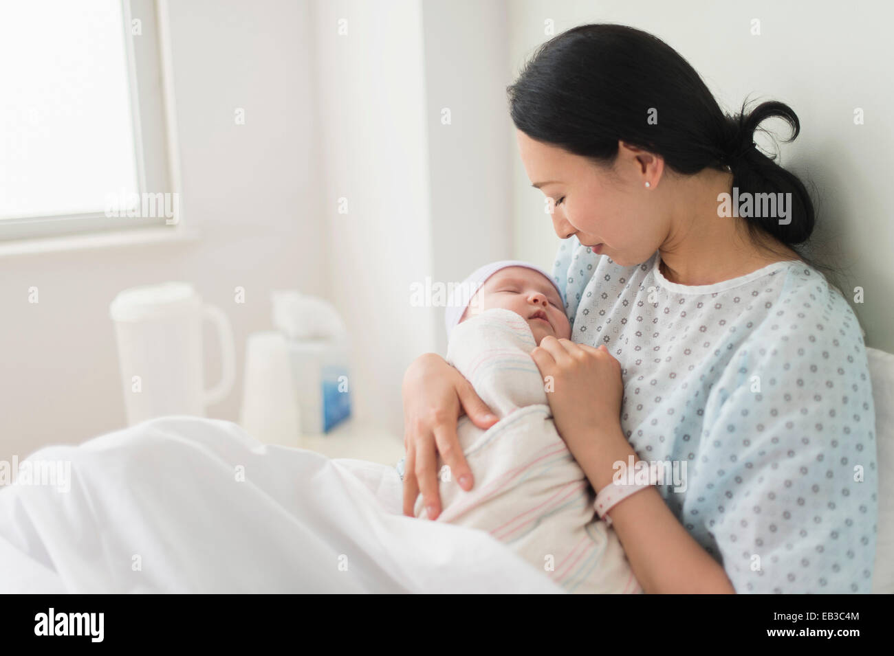 Asian mother holding newborn baby in hospital bed Stock Photo