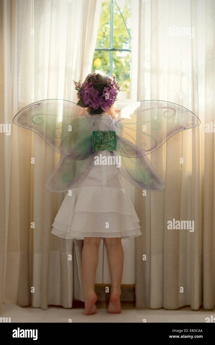 Girl wearing fairy costume looking out of window Stock Photo