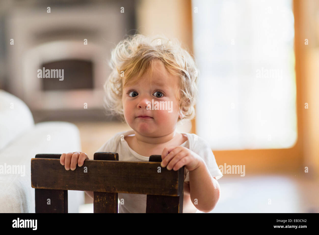 Caucasian baby boy standing behind chair in living room Stock Photo