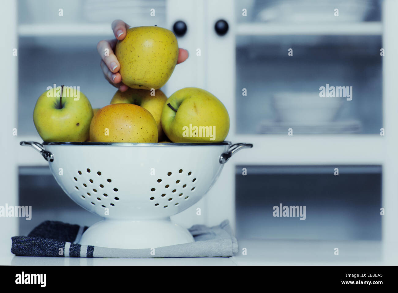 Human hand taking an apple from colander in kitchen Stock Photo