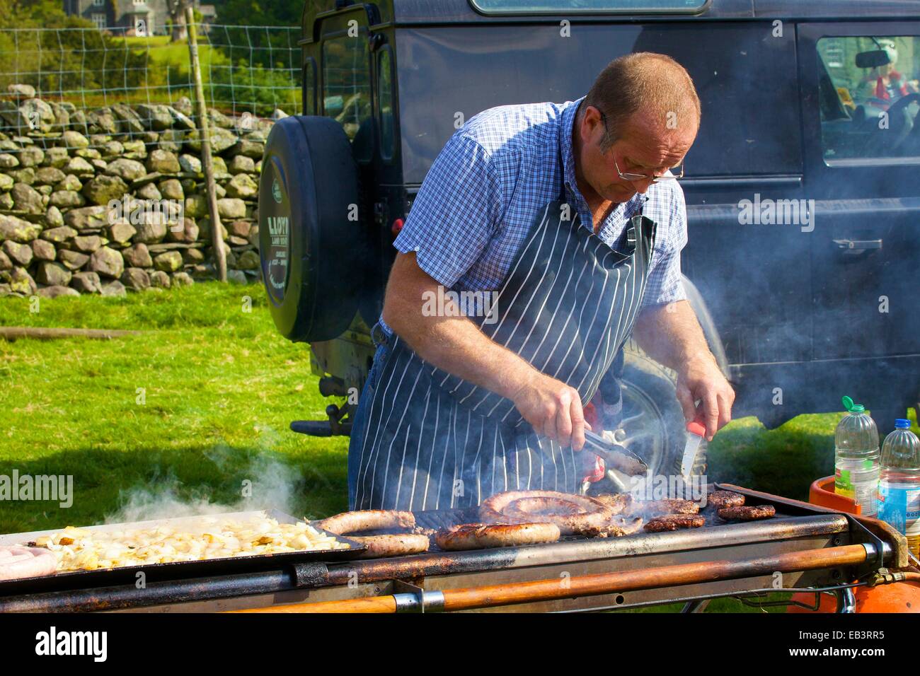 Man frying burgers and sausages at Borrowdale Shepherds’ Meet. Rosthwaite Borrowdale Cumbria England UK. Stock Photo