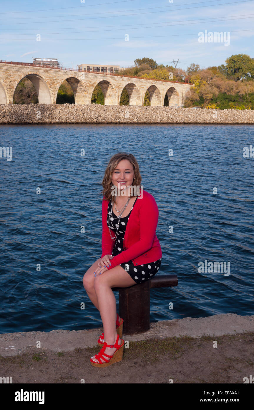 Full length portrait of young teen female outdoors smiling and sitting along Mississippi Riverfront in downtown Minneapolis with Stock Photo