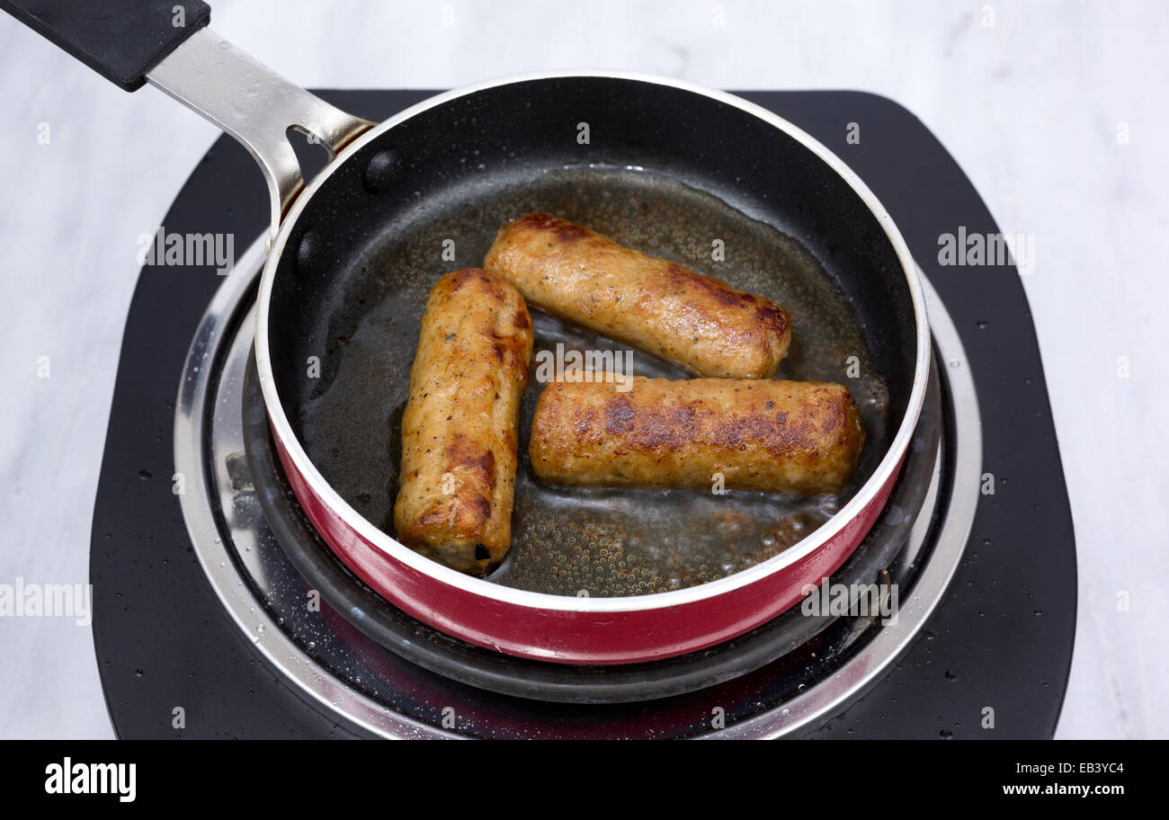 Three breakfast sausages frying in a small skillet atop a single burner stove Stock Photo Alamy