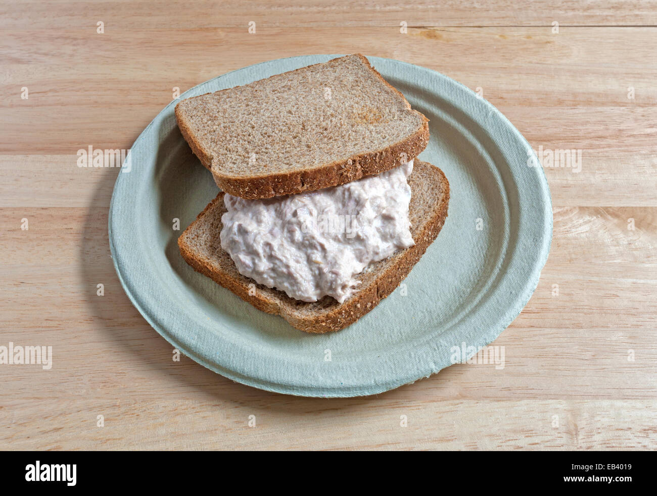 A freshly made tuna sandwich on whole wheat bread on a paper plate atop a wood table Stock Photo
