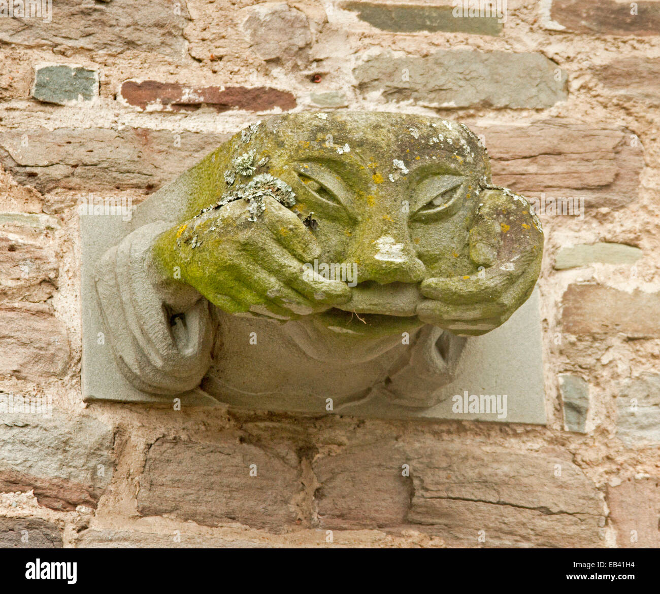 Strange stone gargoyle, on wall at Brecon cathedral in Wales, with hands holding lips up to show open mouth Stock Photo