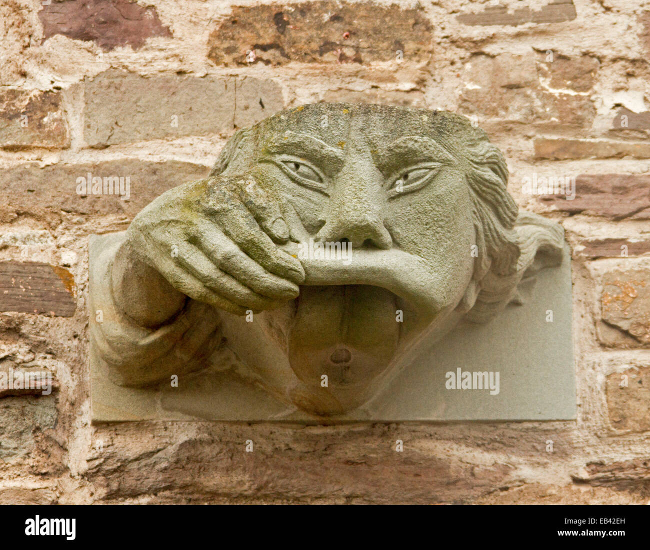 Strange stone gargoyle, on wall at Brecon cathedral in Wales, with hand holding lip up to show mouth wide open Stock Photo
