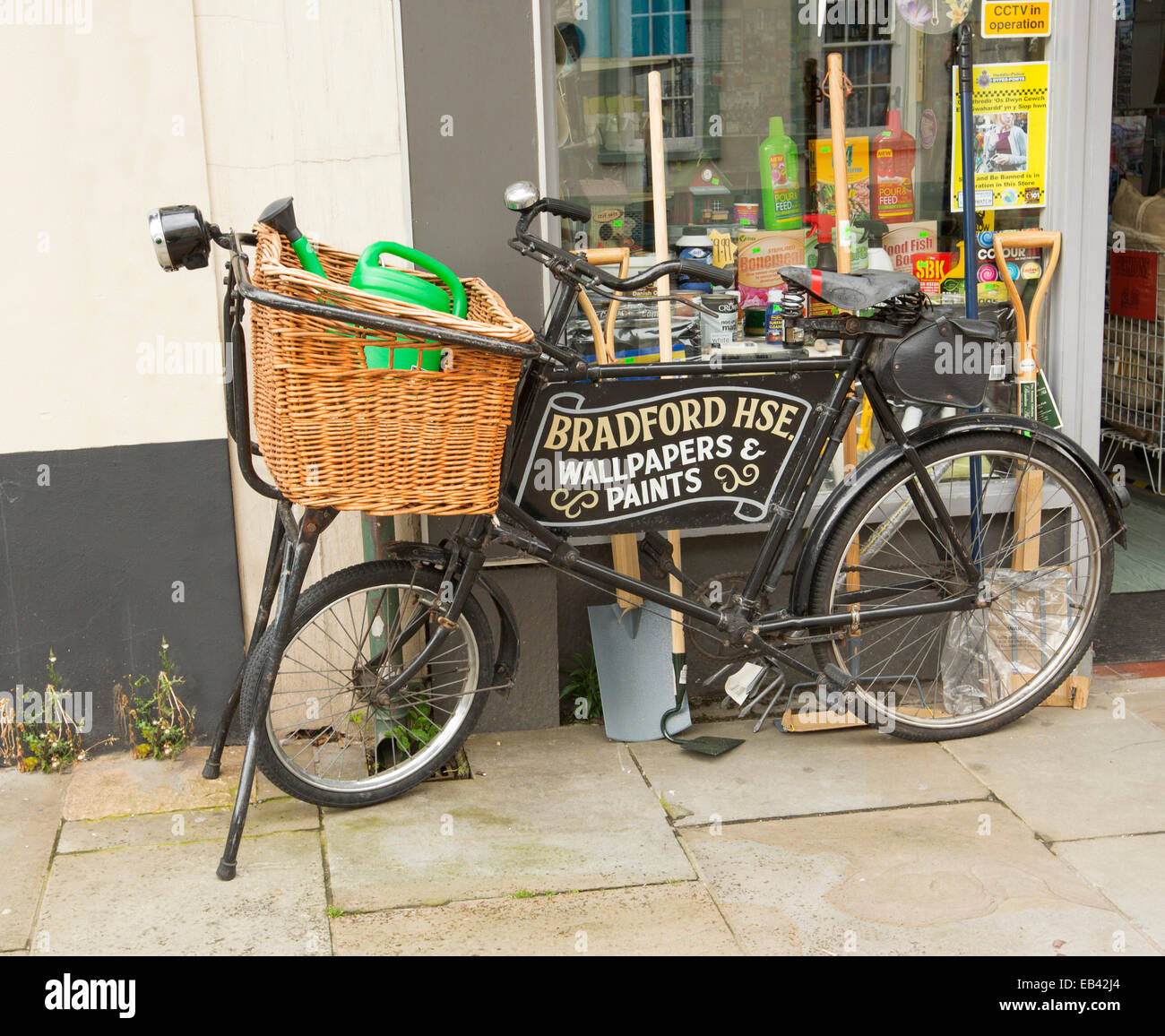 Old black bicycle with grocer's wicker basket & advertising sign built into frame outside hardware shop in Brecon, Wales Stock Photo
