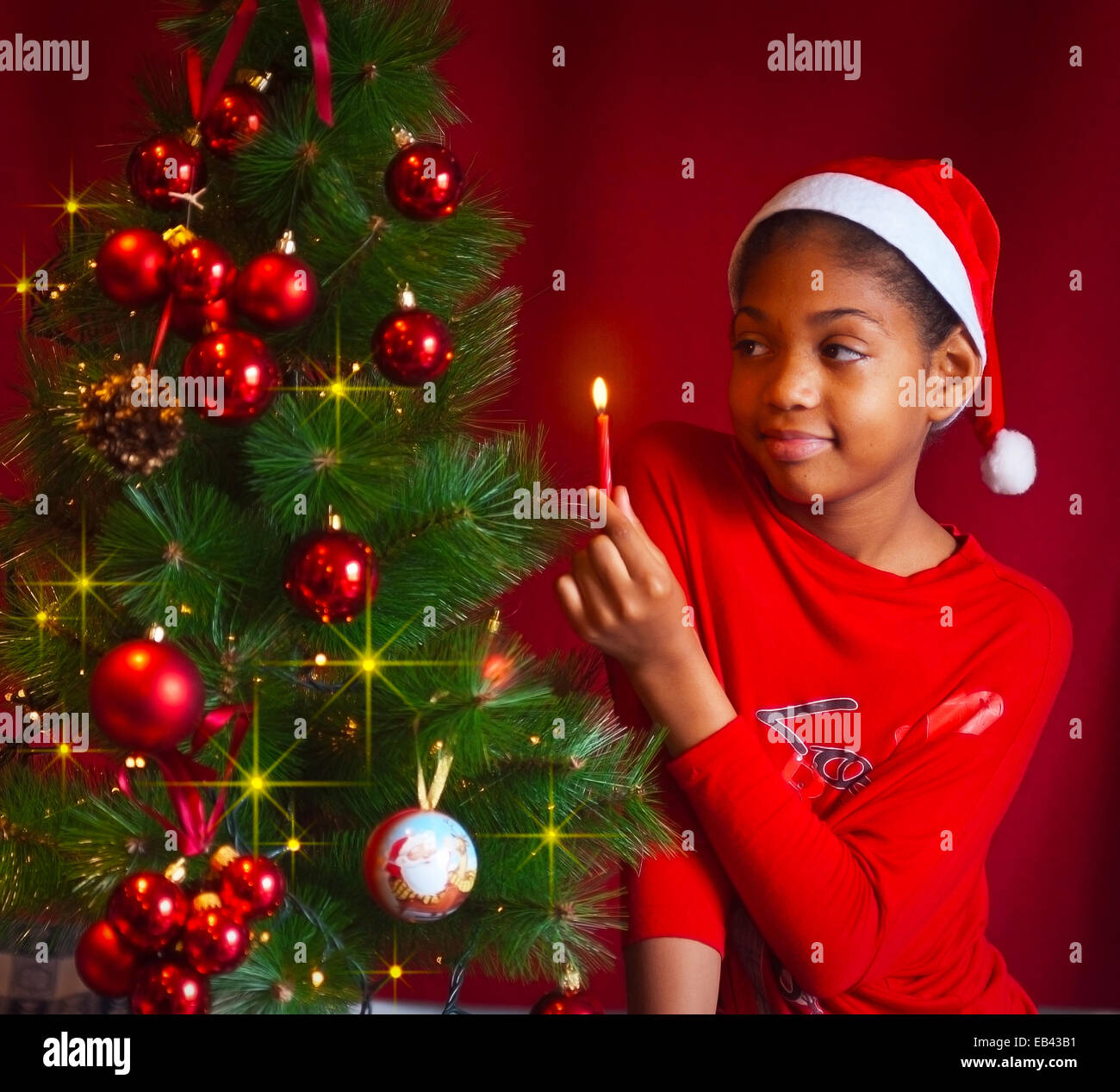 black girl dressed as Santa Claus who decorate the Christmas tree with lights, balls and candles Stock Photo