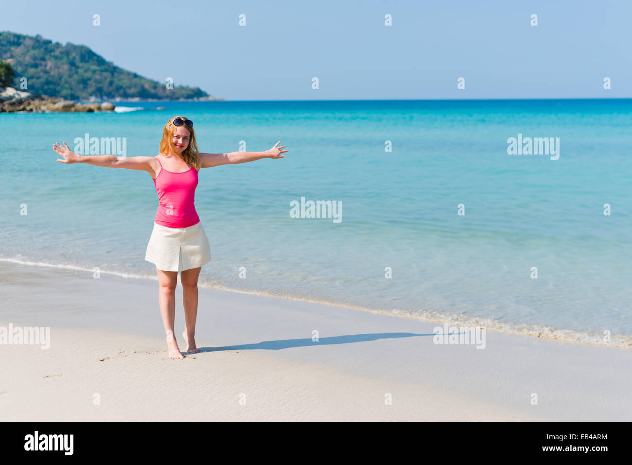 Young woman in pink top and beige skirt walking on beach Stock Photo ...