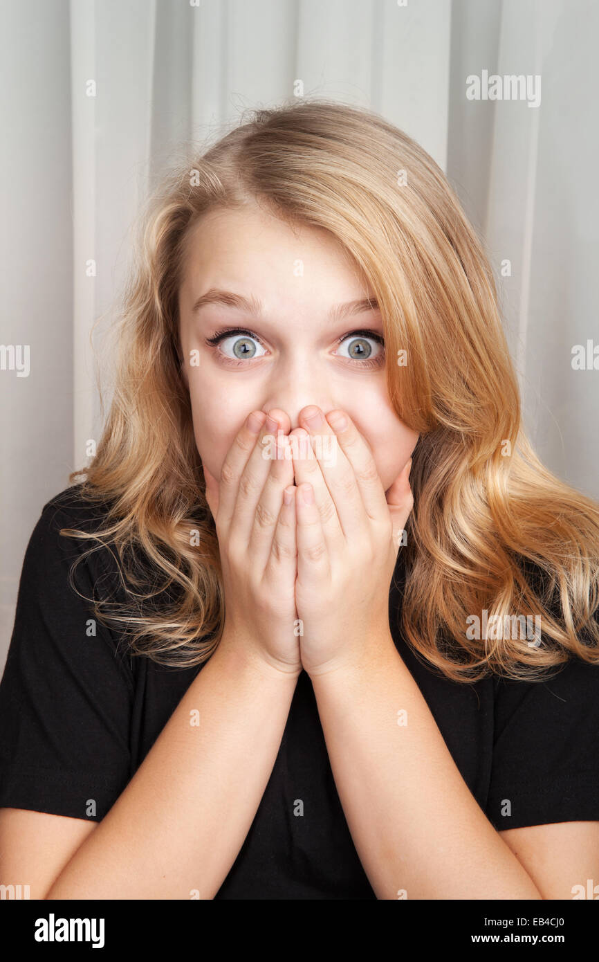 Beautiful blond Caucasian surprised girl opened her eyes wide and covers her mouth with her hands Stock Photo