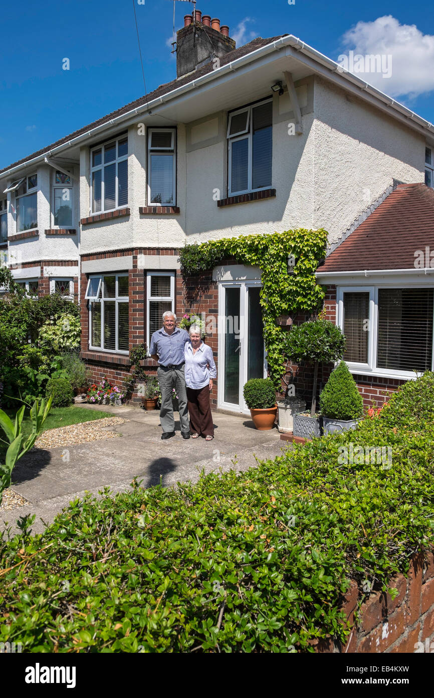 Pensioner couple standing in front of well kept semi-detached suburban house in Cardiff, the capital city of Wales. Stock Photo