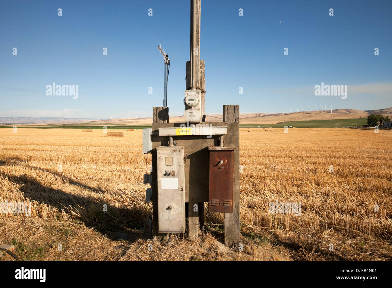 An electrical power meter and distribution panel box in the middle of a farm field near windmill turbines. Stock Photo