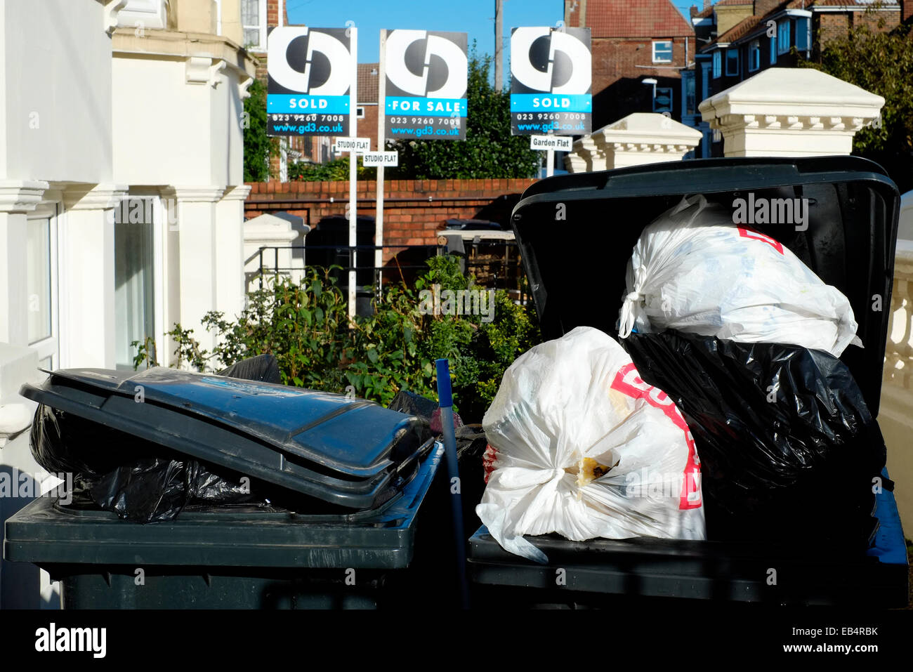 overflowing domestic rubbish wheelie bins await collection from the front garden of an urban house Stock Photo