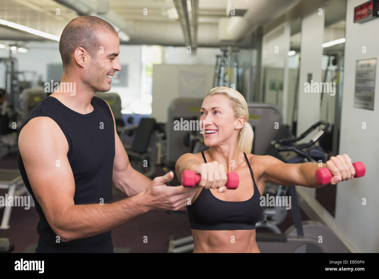 Male trainer assisting woman with dumbbell in gym Stock Photo - Alamy