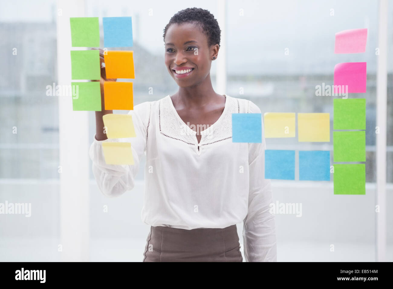 Smiling businesswoman writing on sticky notes on window Stock Photo - Alamy