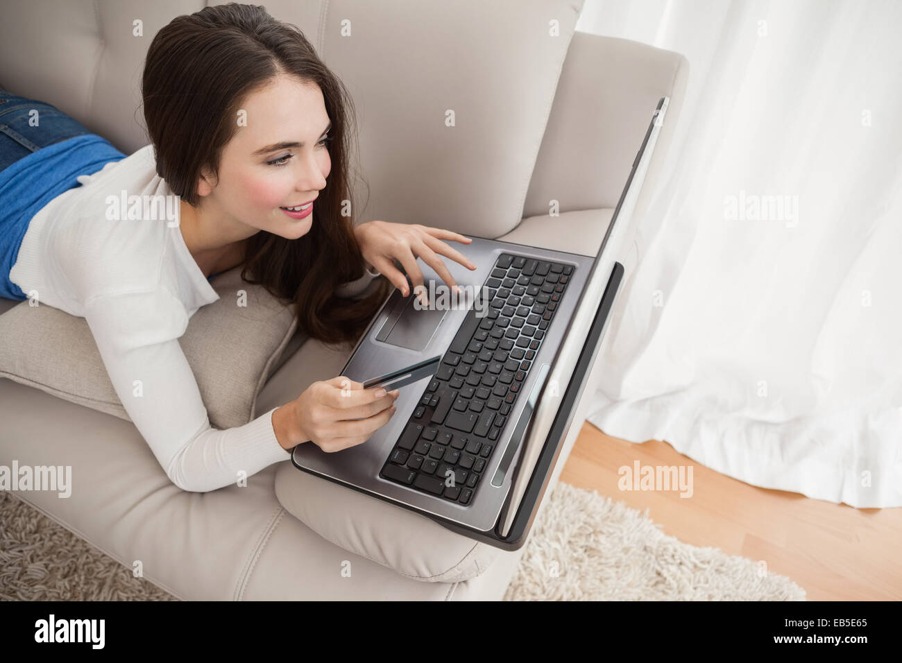 Pretty brunette shopping online on couch Stock Photo - Alamy