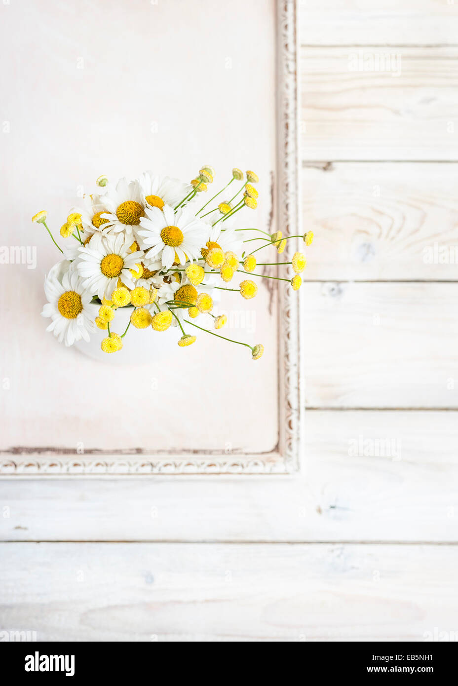 a bunch of ox-eye daisies and tansy flowers in a white vase, on a vintage ivory painted wooden tray on white wooden board Stock Photo