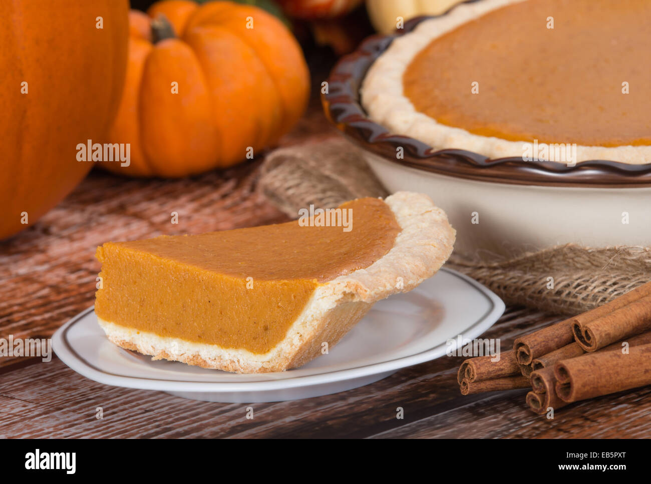 Slice of a pumpkin pie on wooden table. Pie and pumpkins on the background. Stock Photo