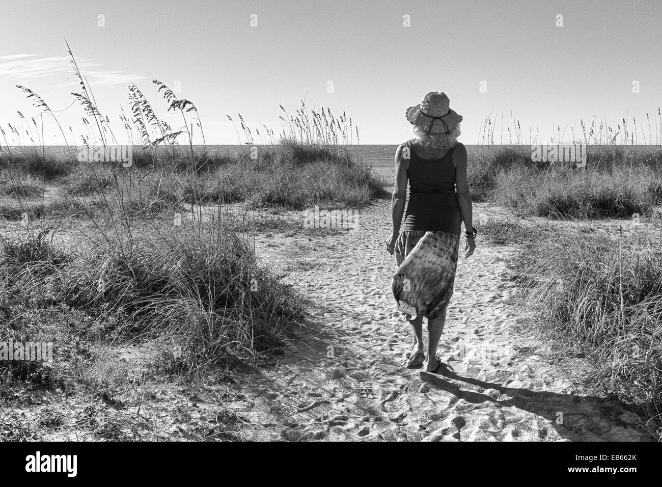mature woman is walking down a path toward the beach.  Vacation. Stock Photo