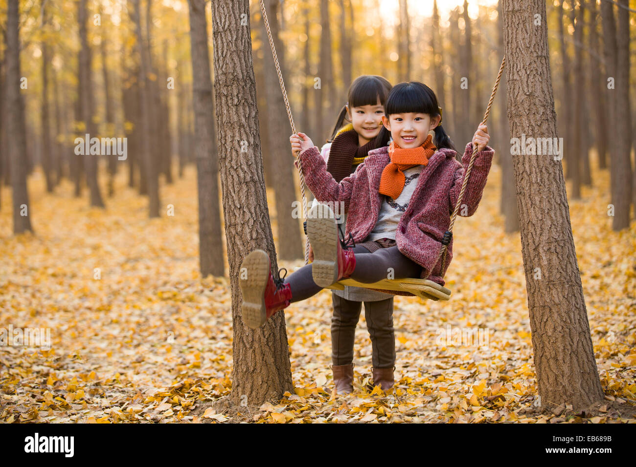 Little girl pushing her sister on a swing in autumn woods Stock Photo