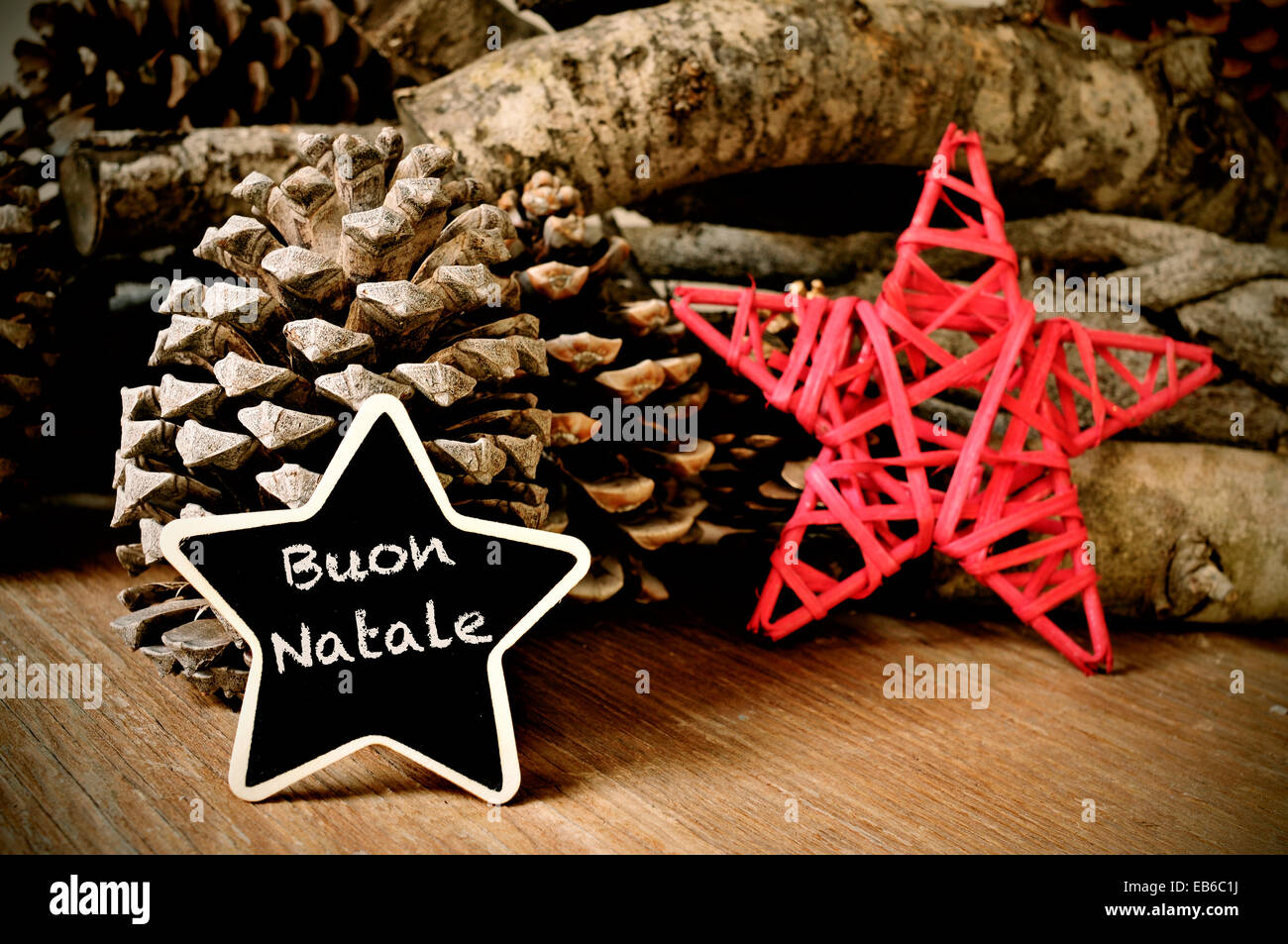 the text buon natale, merry christmas written in italian in a star-shaped blackboard, and a christmas star, some pinecones and a Stock Photo