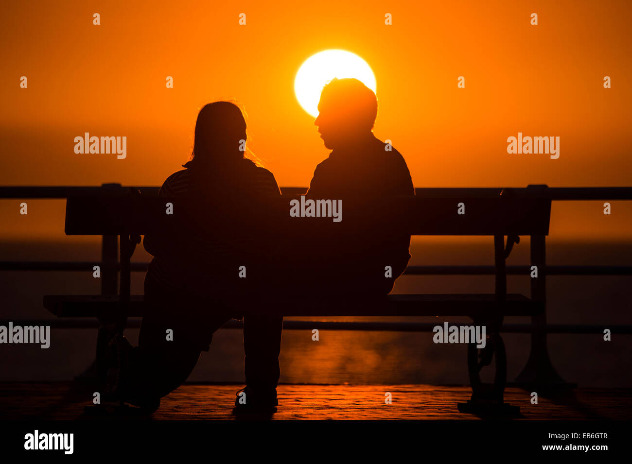 A couple sitting on a seaside bench in silhouette at sunset, September ...