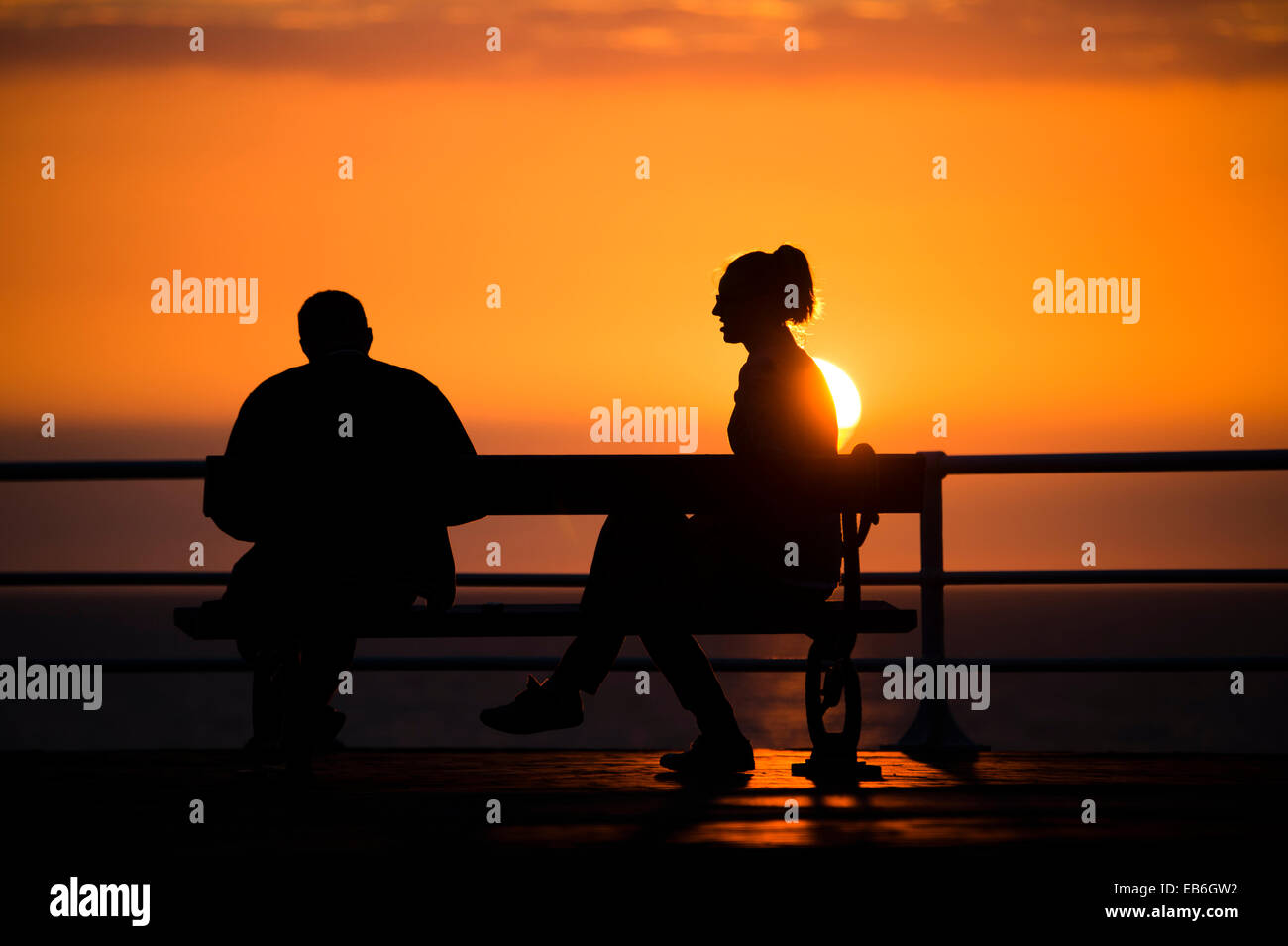 A couple sitting on a seaside bench in silhouette at sunset, September ...