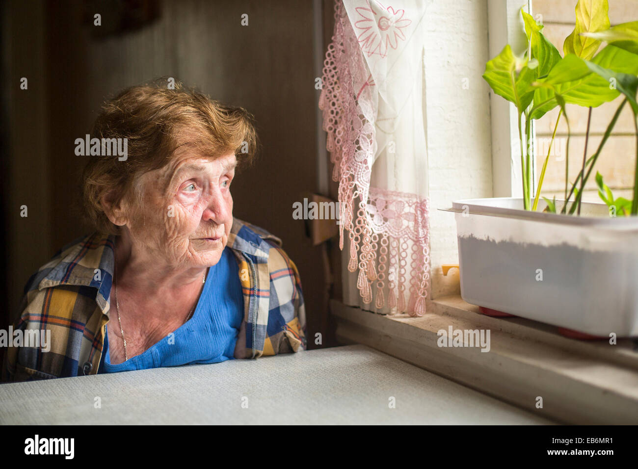 Old woman sitting alone near the window in his house. Loneliness in old age. Stock Photo