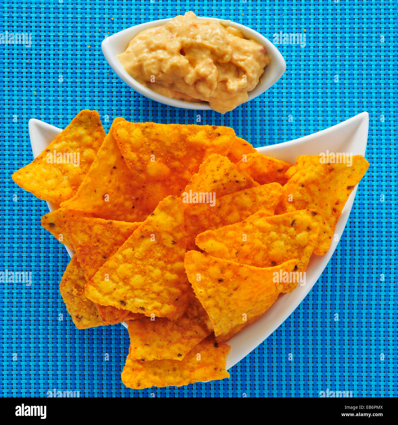 a plate with tortilla chips and a bowl with hummus, on a blue fabric background Stock Photo
