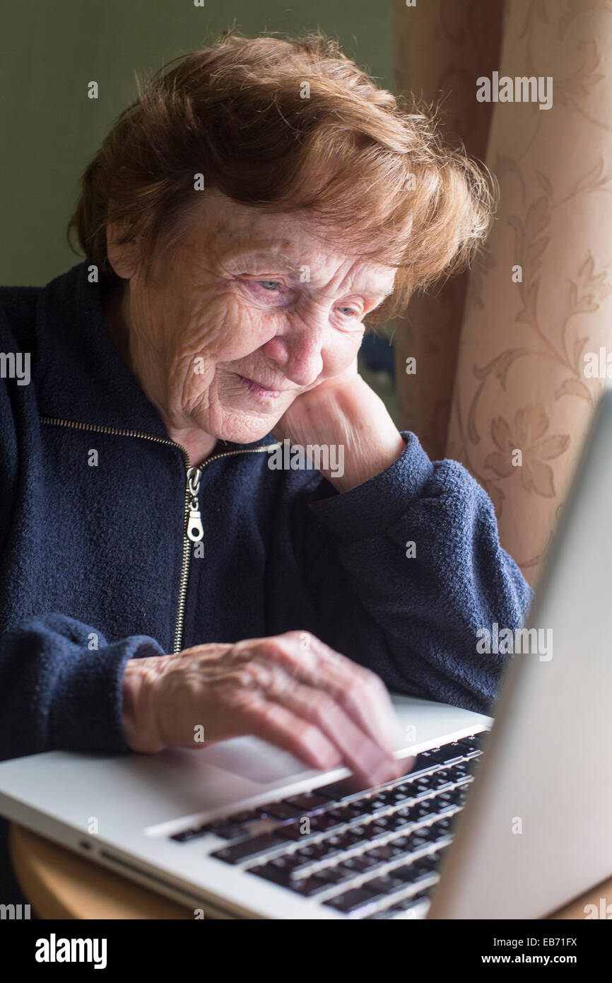 Old woman working on a laptop at his home. Stock Photo