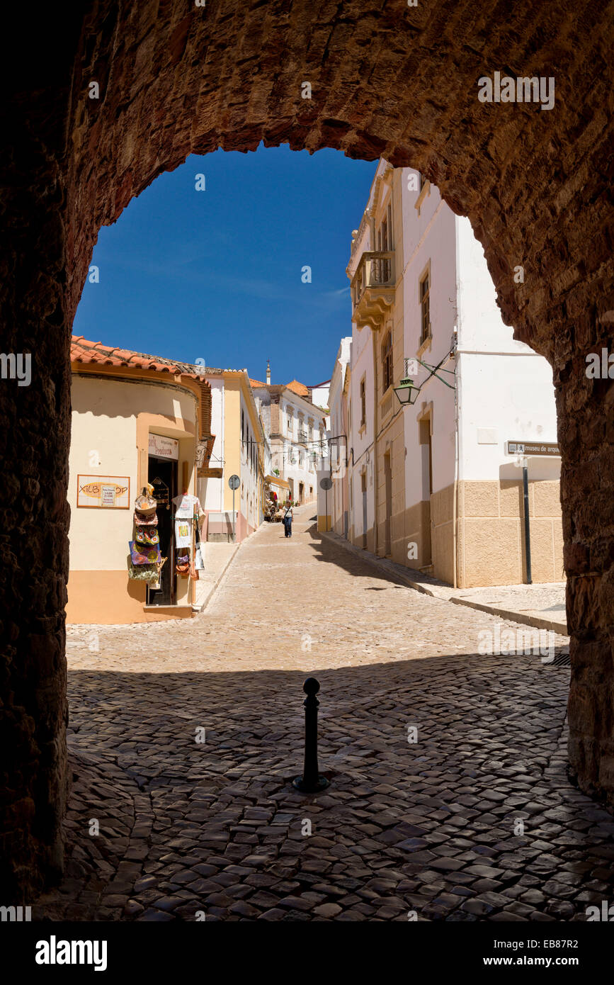 Portugal, the Algarve, Silves, a narrow cobbled street in the old town seen through an archway in the city walls Stock Photo
