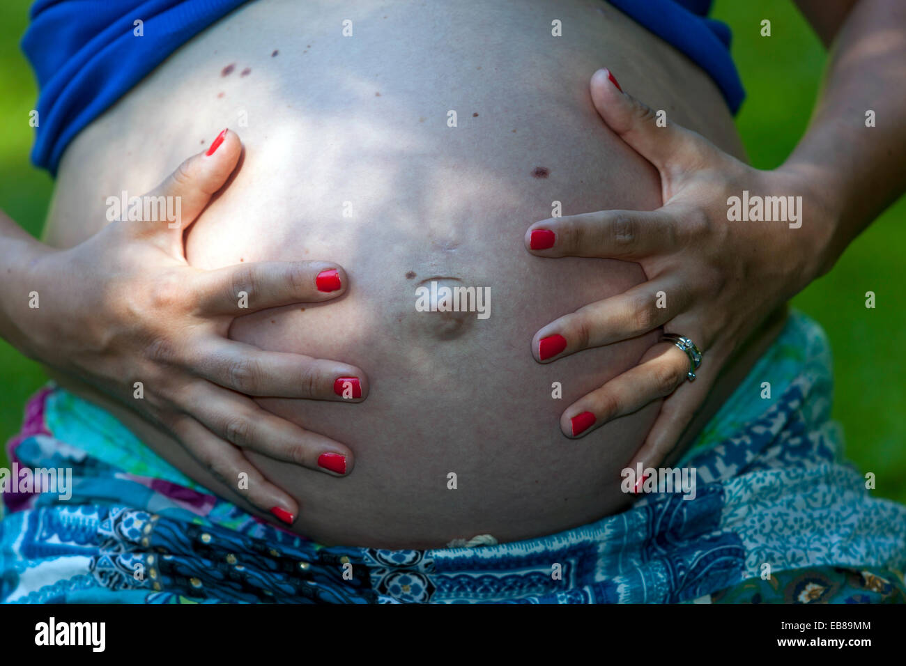 Pregnant woman belly, toes painted red nails, fingers Stock Photo