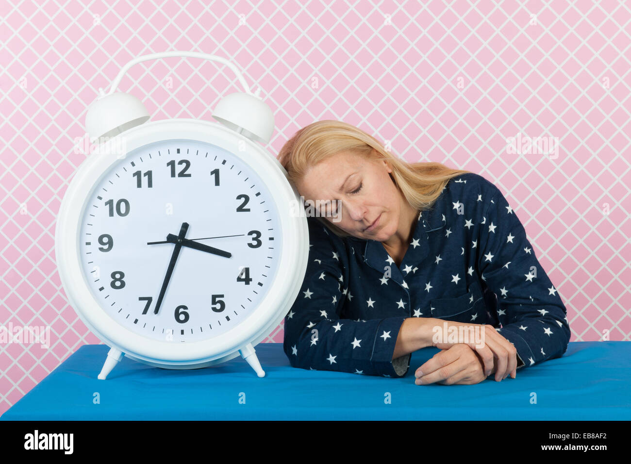 Woman of mature age laying next to big alarm clock Stock Photo