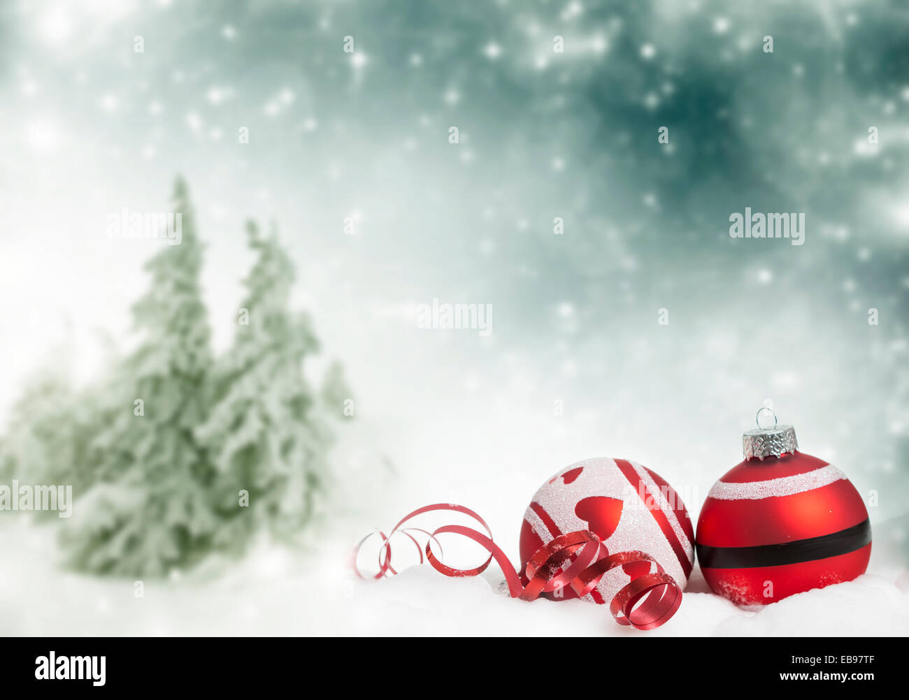 Red Christmas decorations in front of snow cowered pine trees Stock Photo