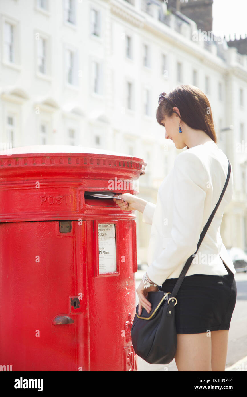 Young Woman Mailing Letter in Red Postbox, London, England, UK Stock Photo