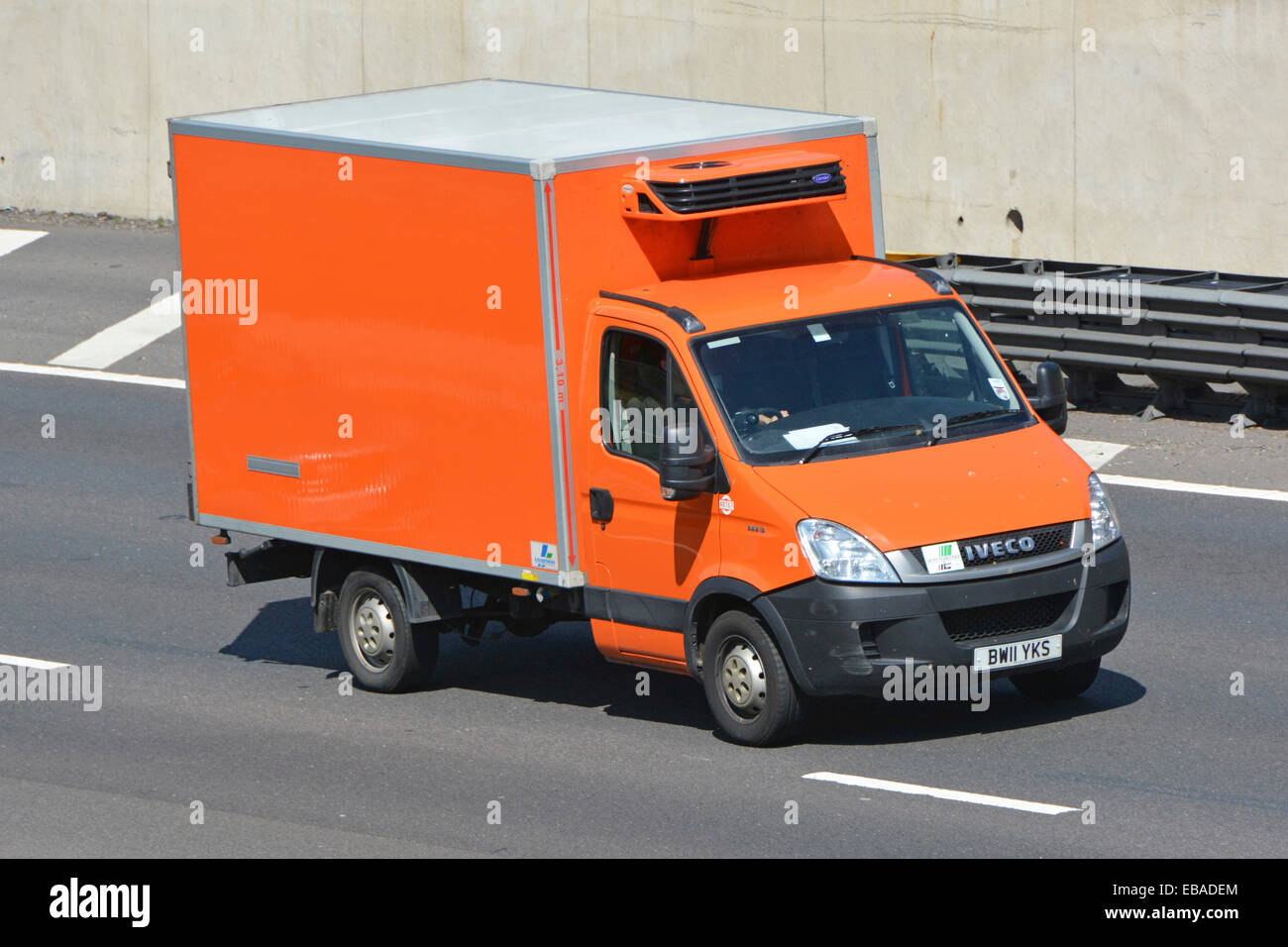 Orange coloured clean unmarked Iveco van fitted with Carrier cooling unit driving along M25 motorway Stock Photo