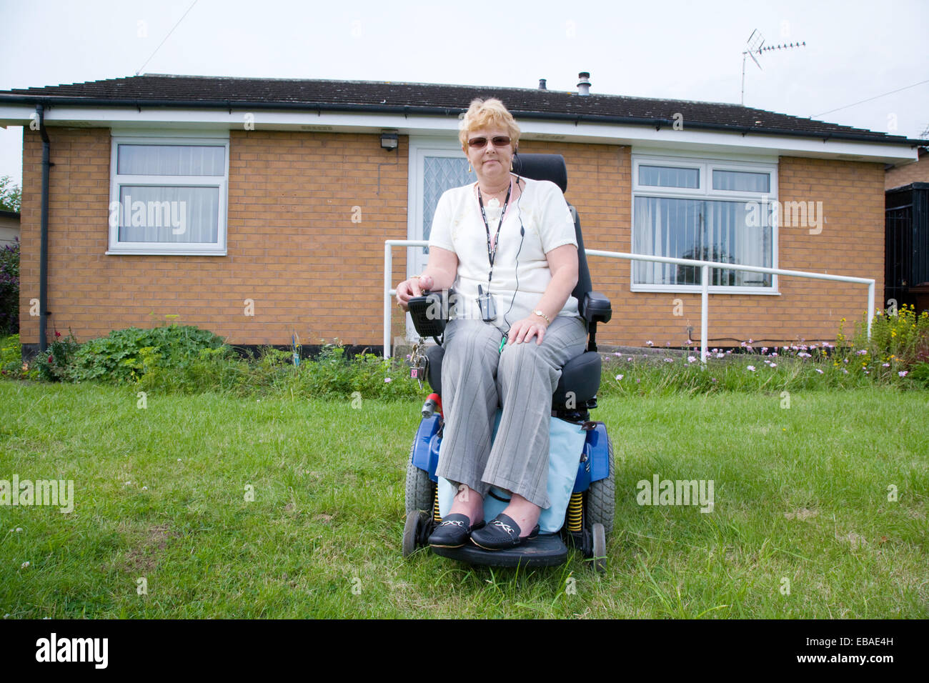 Female wheelchair user outside her house; concrete ramp and grab rails