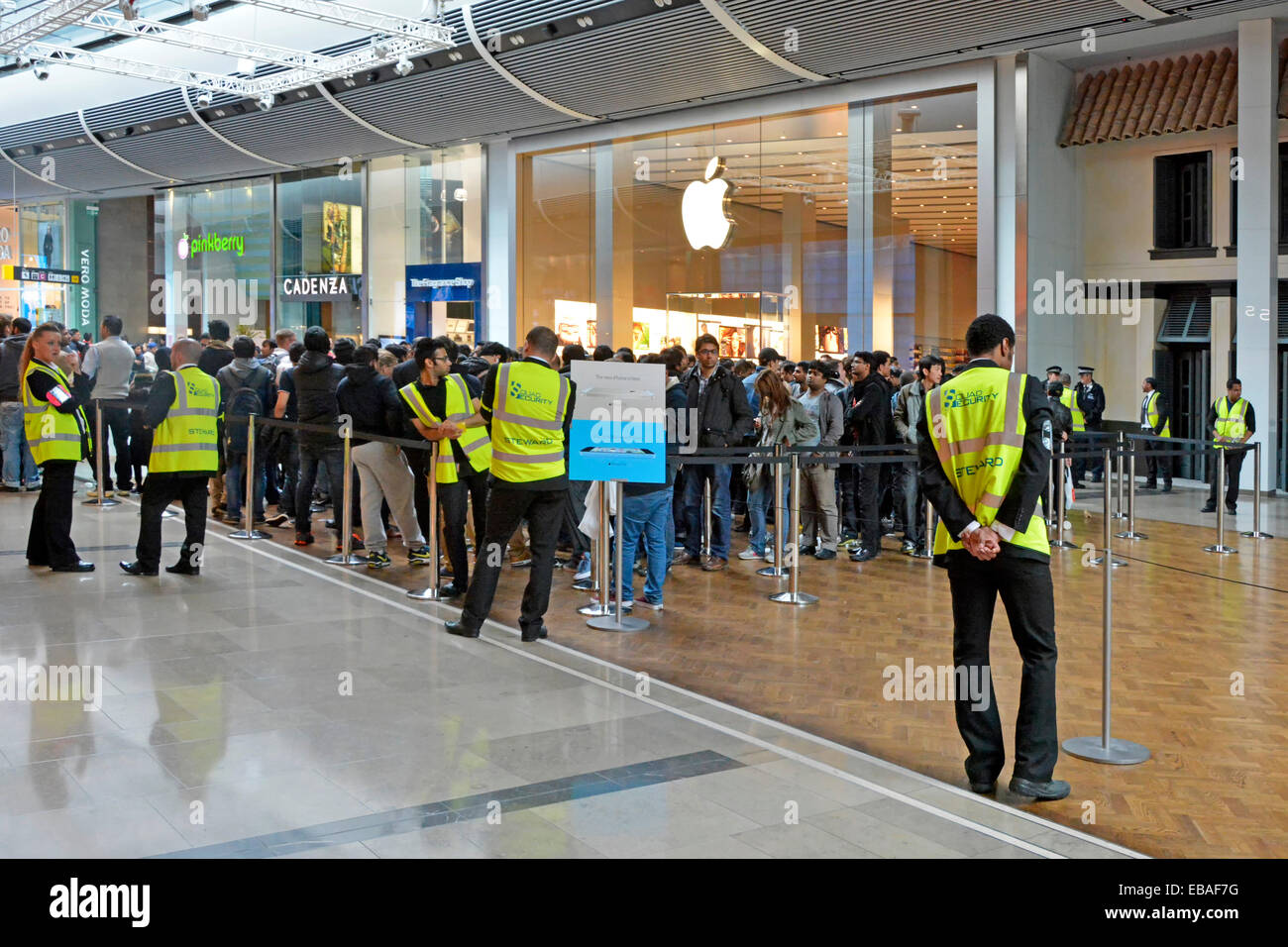 Security staff supervising crowds of people outside retail Apple business store interior Westfield shopping centre mall Stratford Newham East London Stock Photo