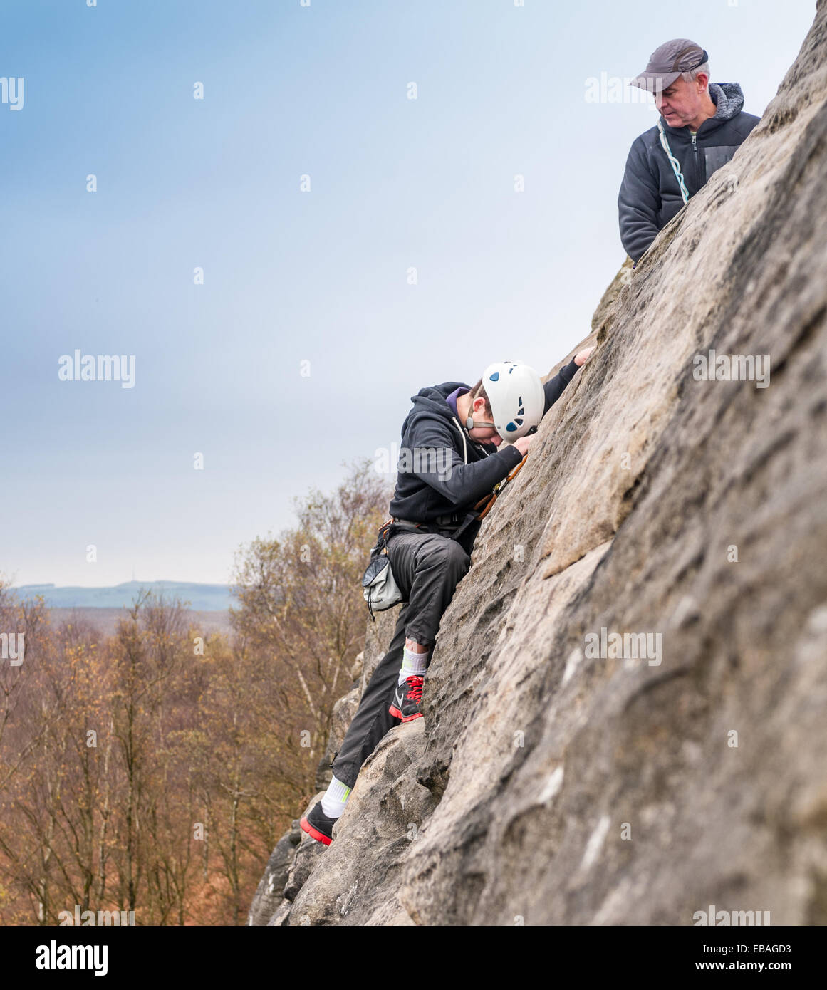 Young rock climber on Birchen Edge in The Peak District of Derbyshire - with an instructor guiding a teenage boy up the rock Stock Photo