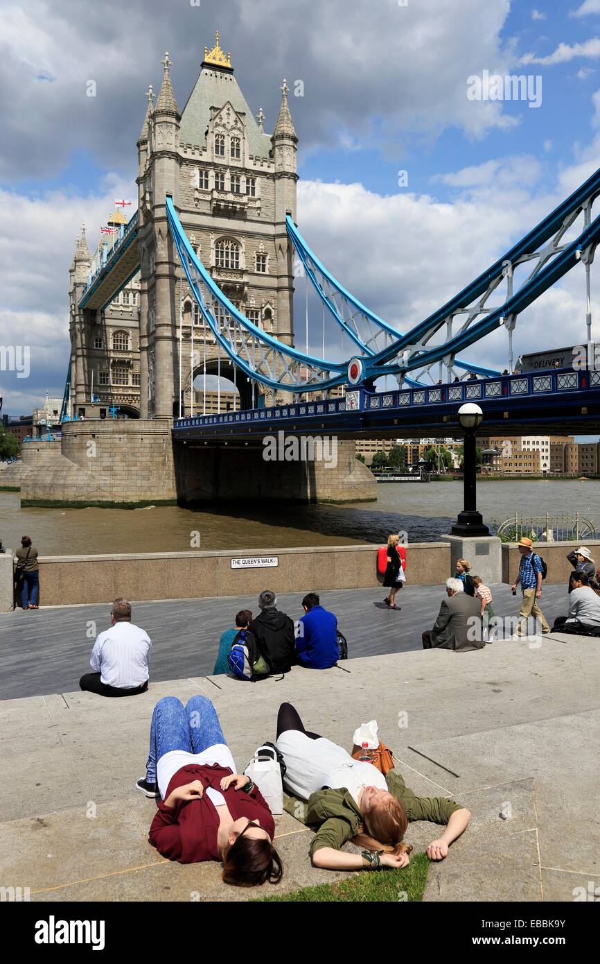 Two young women taking sunbathing on bank of River Thames with Tower Bridge in the background. London. England. United Kingdom. Stock Photo