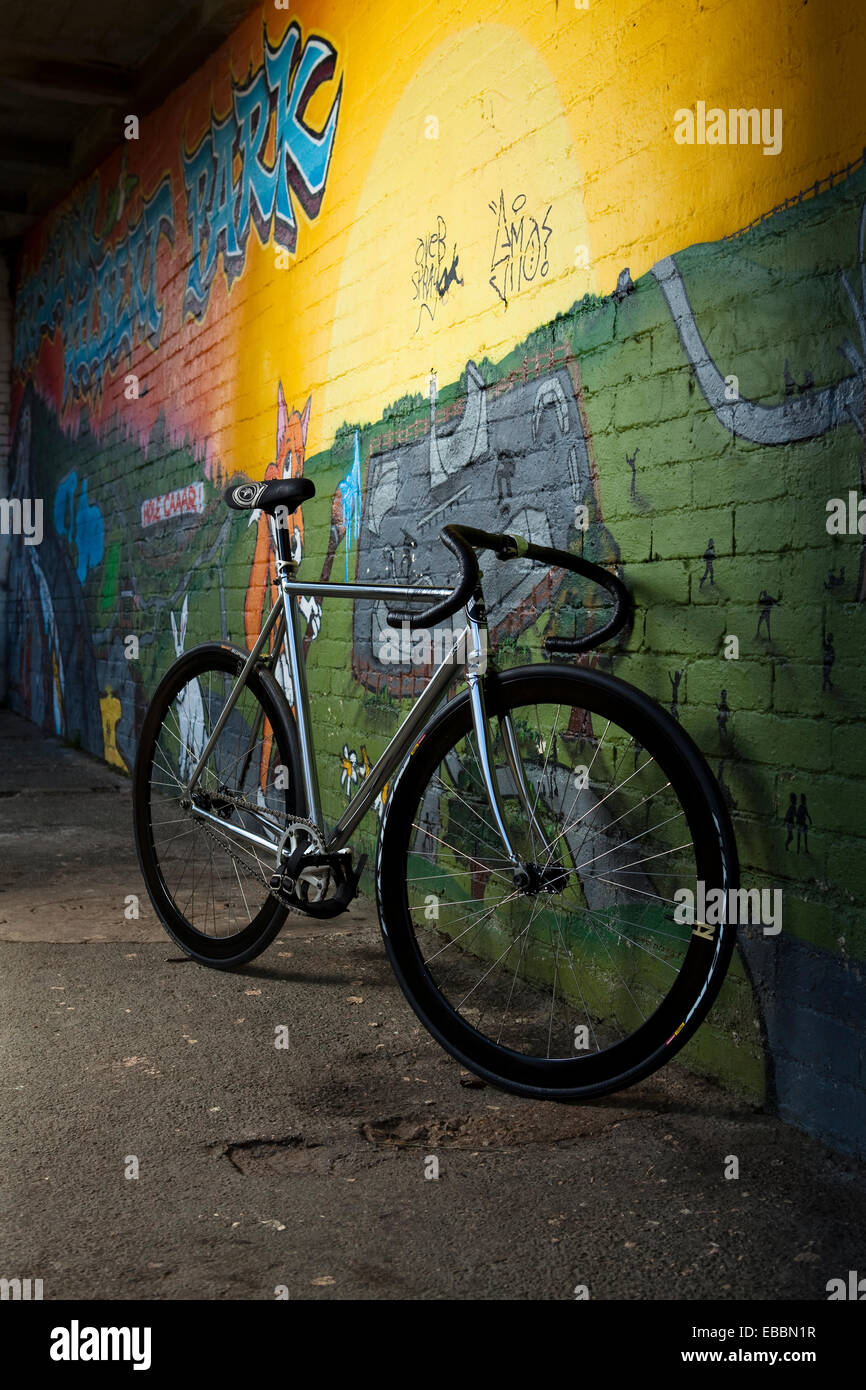 A fixed-gear bicycle lent against a colorful graffiti-covered wall. Stock Photo