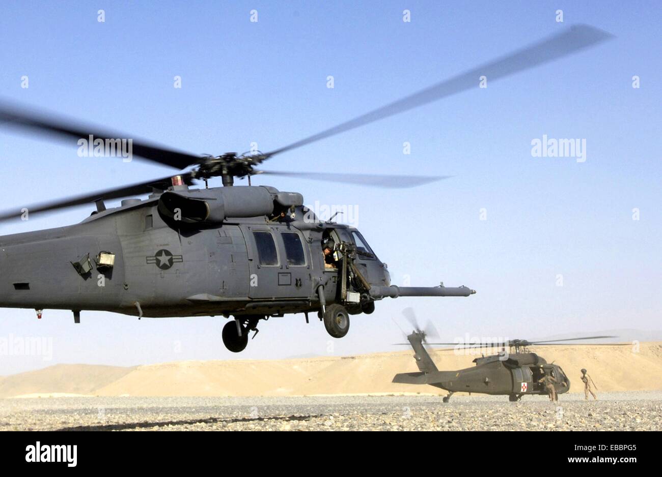 An HH60 Pave Hawk helicopter lands as an Army UH60 Blackhawk prepares