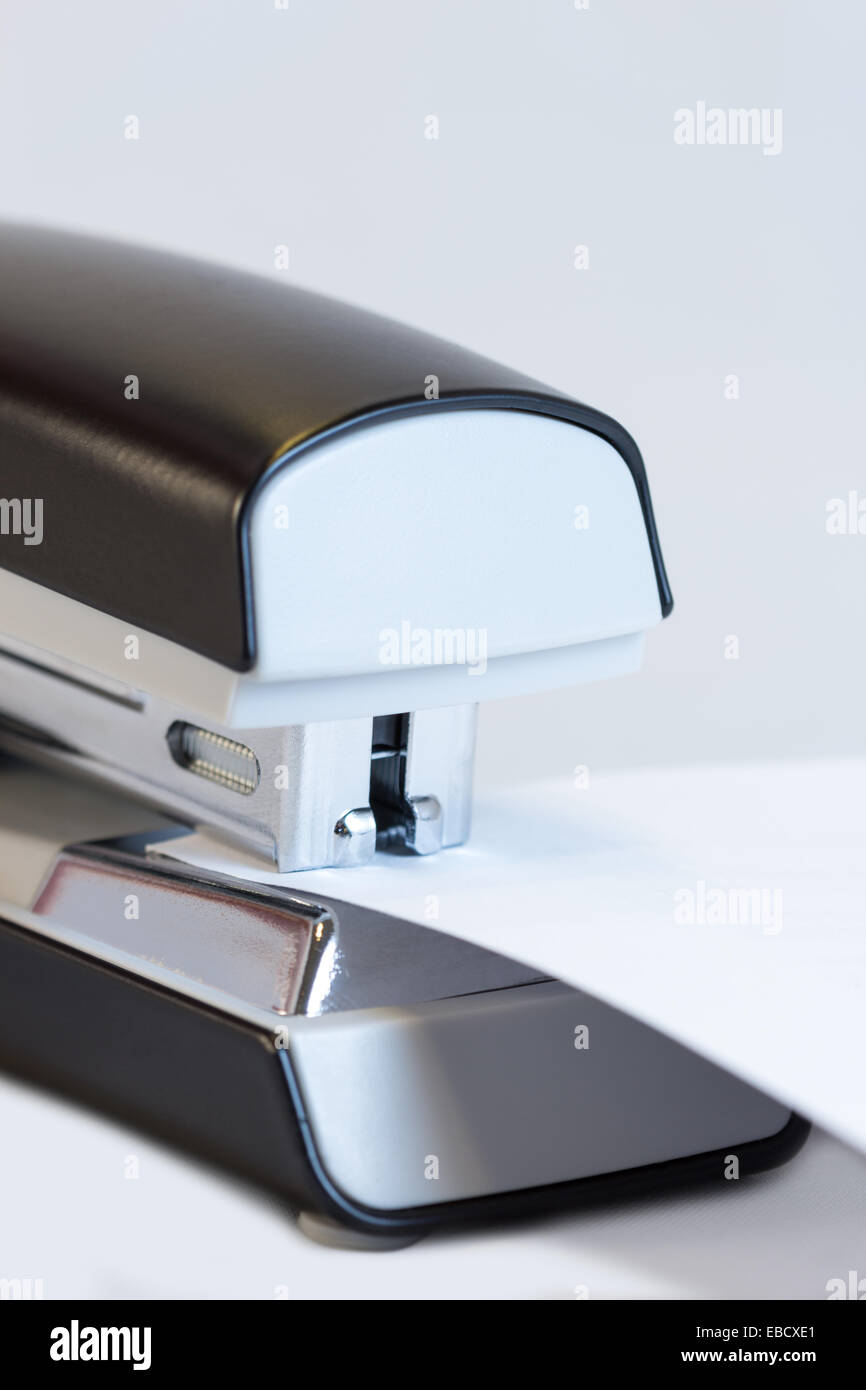Closeup of a grey office stapler stapling white paper Stock Photo