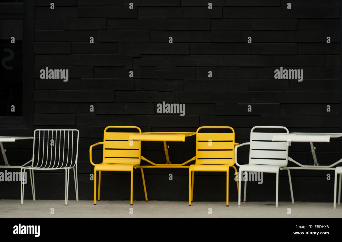 A row of yellow and white chairs separated by small tables outside a