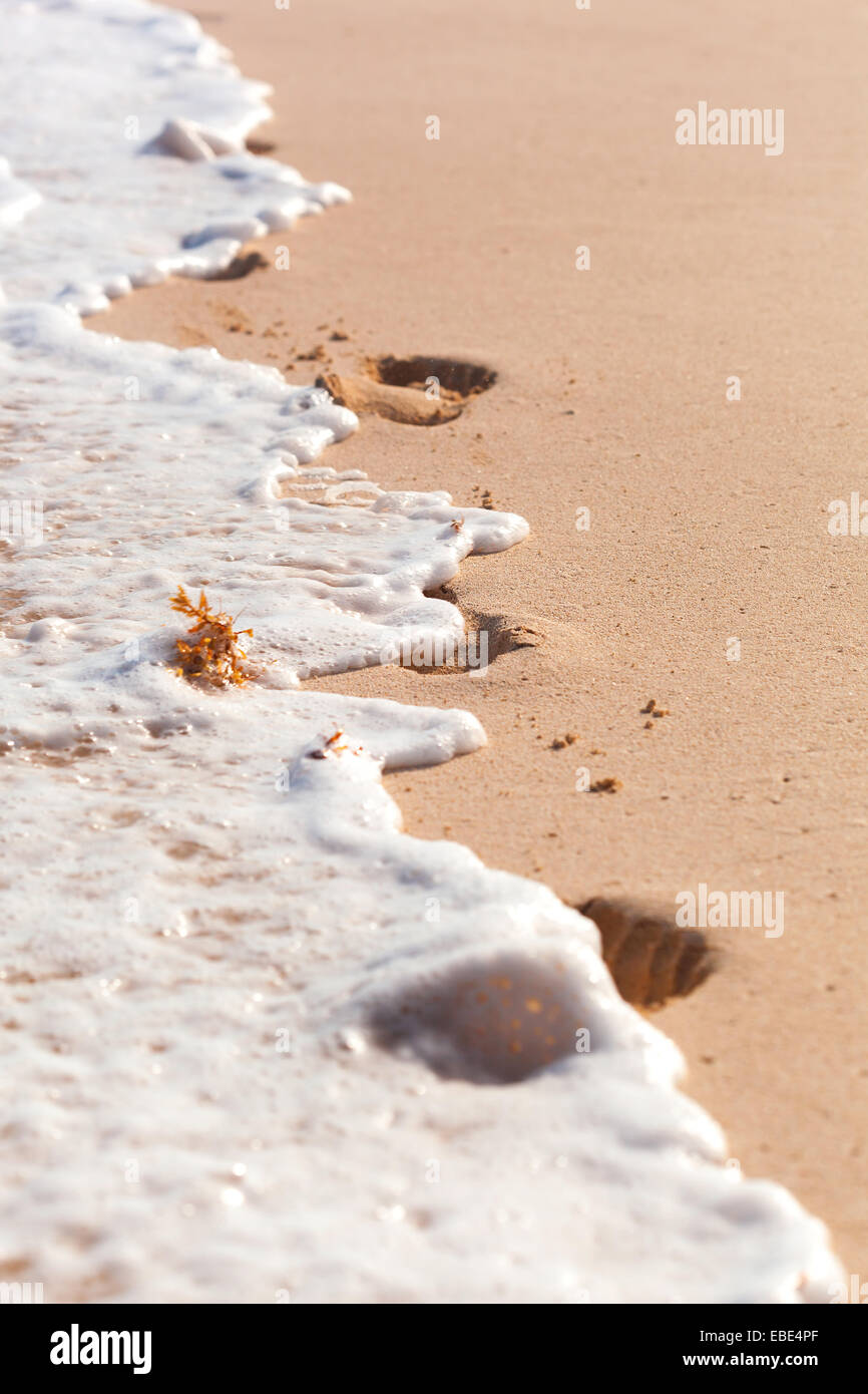 Footprints in foamy waves washing away Stock Photo