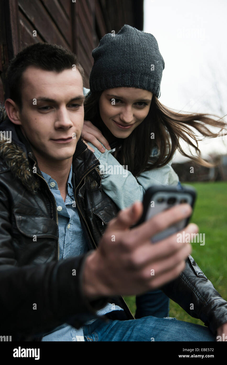 Close-up of young man and teenage girl outdoors, looking at cell phone ...