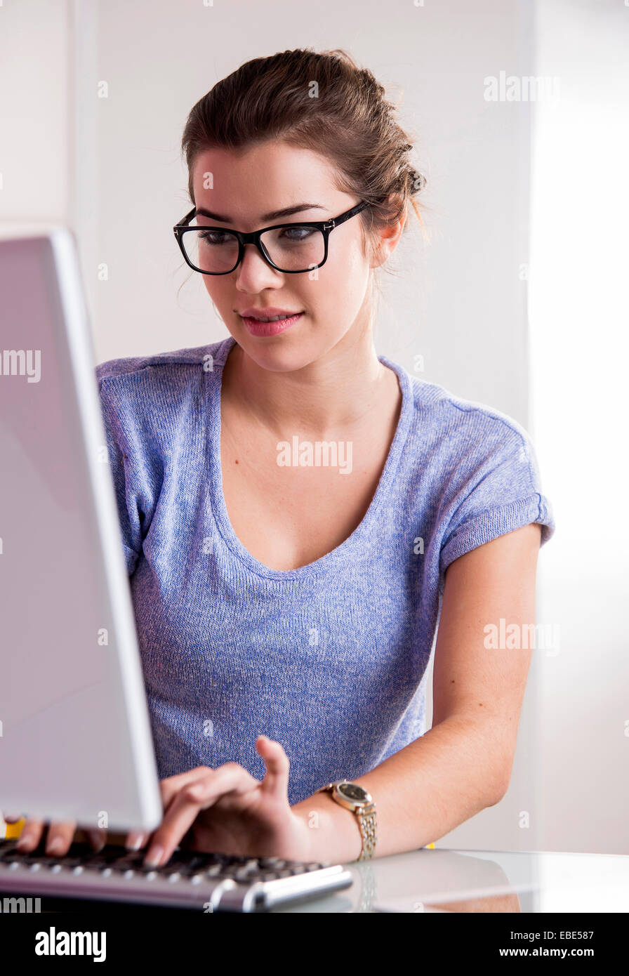 Young woman wearing horn-rimmed eyeglasses, working in office on desktop PC, Germany Stock Photo