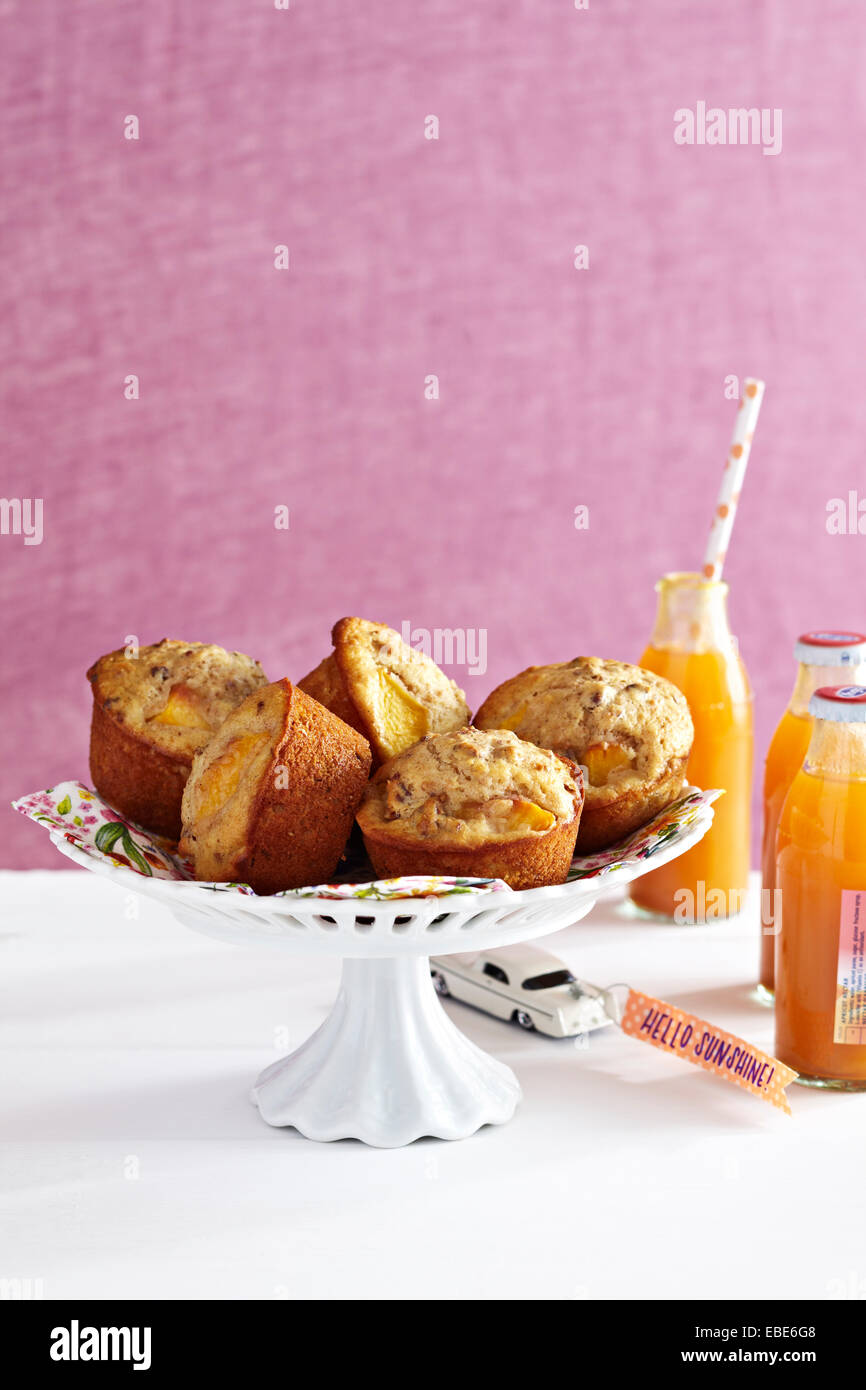 Peach Muffins on Cake Stand with Bottles of Juice with Pink Background, Studio Shot Stock Photo