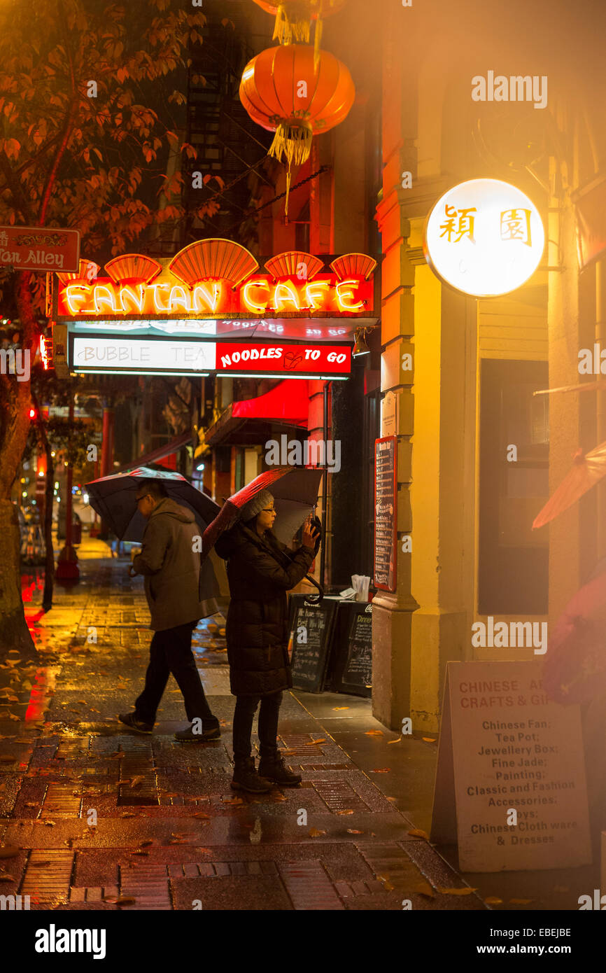 Chinese couple at Fan Tan alley entrance in Chinatown on rainy night-Victoria, British Columbia, Canada. Stock Photo